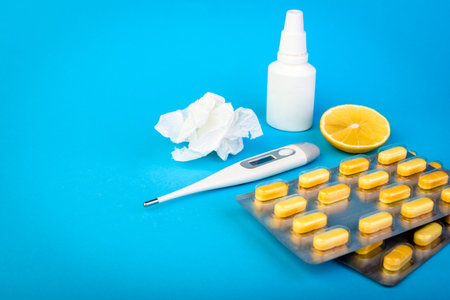Various medicines, lemon, thermometer, sprays from stuffy nose and pain in throat on blue background. Treatment of colds and flu.の写真素材