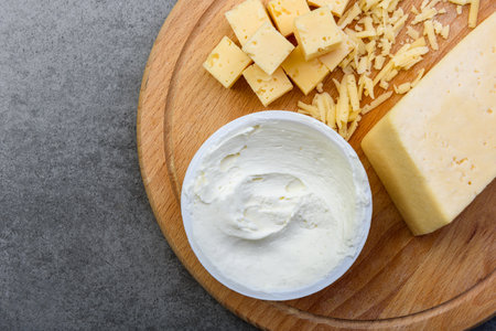 Sliced cheese cubes and cream cheese on wooden board on gray background.の写真素材