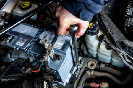 A man installing a new car battery under the hood of a car. Vehicle maintenance and repair.の写真素材