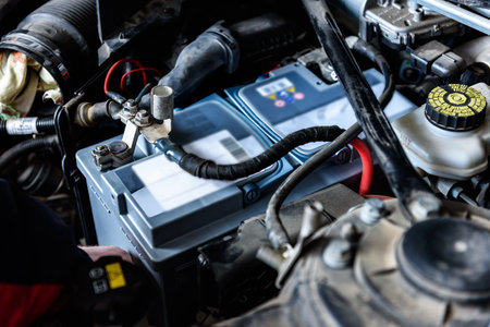 A man installing a new car battery under the hood of a car. Vehicle maintenance and repair.