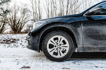 Very dirty salty black car is parked on nature covered by snow in winter.の写真素材