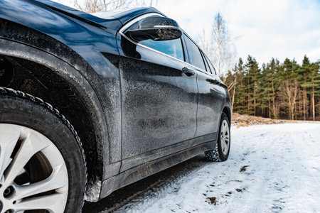 Very dirty salty black car is parked on nature covered by snow in winter.の写真素材