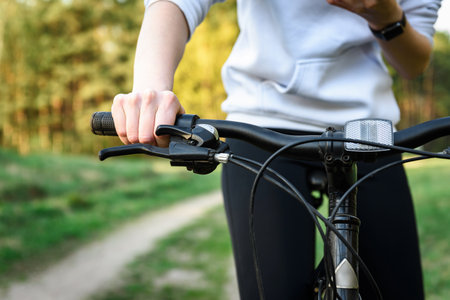 Woman cyclist holding handlebars of mountain bike outdoors on spring forest background.