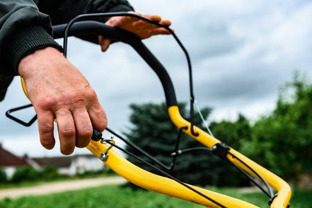 A man starts the engine of a petrol lawn mower with a starter rope. Mowing grass in summer.