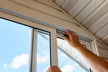 Installing and adjusting white sliding metal-plastic window using screwdriver on a balcony in a...