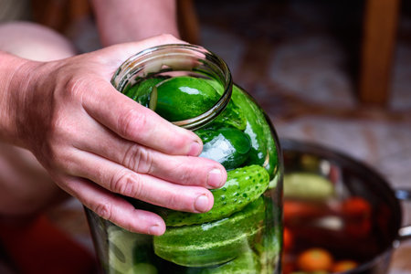 Preservation of seasonal vegetables. Woman putting washed cucumbers in a glass jarの写真素材