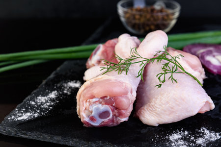 Raw chicken legs with spices on black backgroundの写真素材