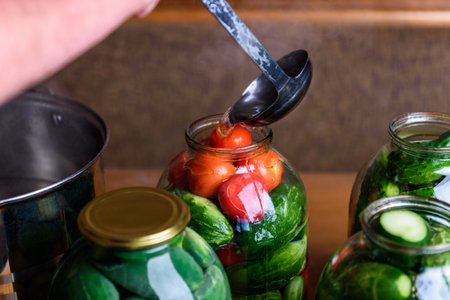 Preservation of seasonal vegetables. A woman pouring the prepared marinade into jars with cucumbers...