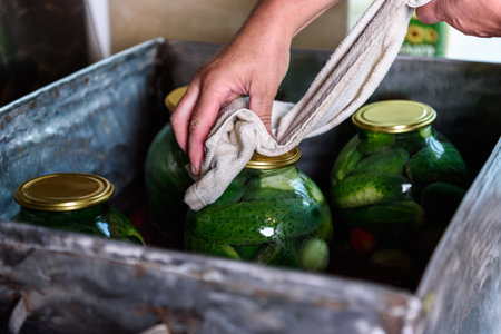 Preservation of seasonal vegetables. A woman sterilizing jars of cucumbers and tomatoes in a large barrel in the kitchenの写真素材
