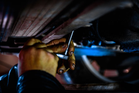 A car mechanic installing and screwing a new oil filter under the car using a wrenchの写真素材