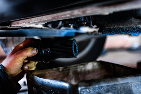 A car mechanic draining the old motor oil and removing the old oil filter under the car.の写真素材