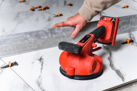Tiler laying tiles on wall using electric vibrating suction cup