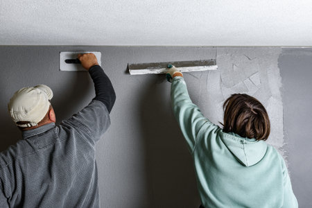 Workers applying and smoothing decorative pebble plaster using a putty knife and float on a wall.の写真素材