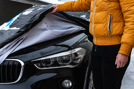 The driver opening the car protected from the weather by a tarpaulin cover in winterの写真素材