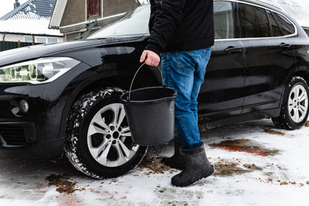 Man hand-washing black car using brush and bucket in winterの写真素材