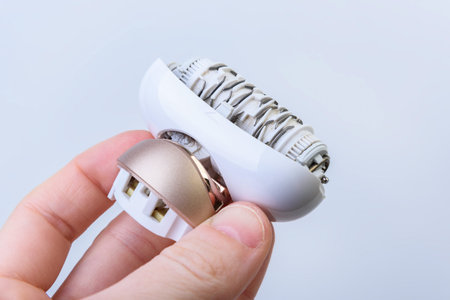 Woman holding and cleaning an electric epilator from hair with a brush on gray background. Maintenance of equipmentの写真素材
