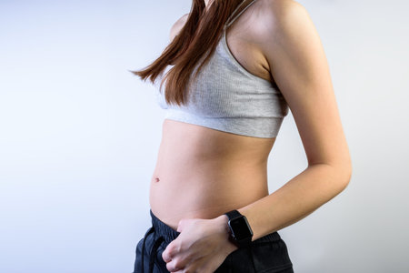 A young girl with a big belly on a gray background. Side view