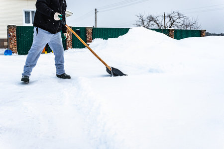 Man shoveling snow from walkway in his yard using plastic snow shovel on winter dayの写真素材