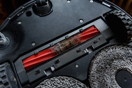 A woman's hands remove tangled hair in a robot vacuum cleaner brush. Care and maintenance of...