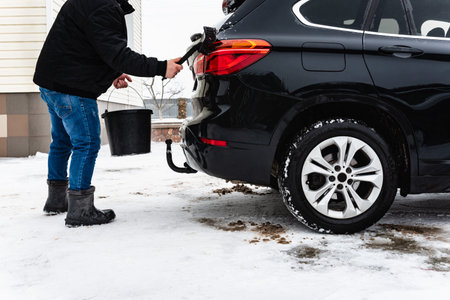 Man hand-washing washing black car from dirt and salt using a brush and bucket in winter