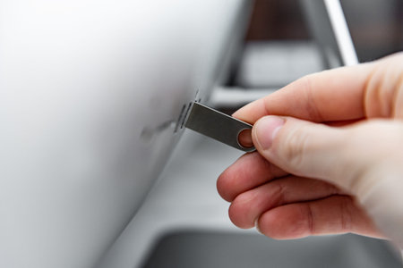 Hand holding silver USB flash drive connected to on the back of the monoblockの写真素材