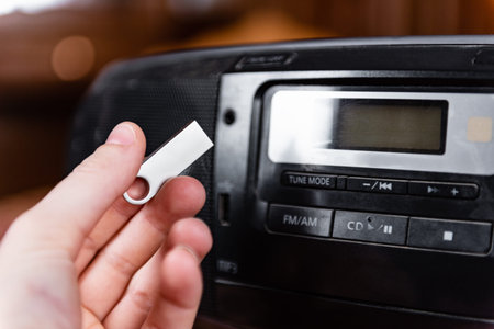 Hand holding silver USB flash drive connected to audio system or tape recorder
