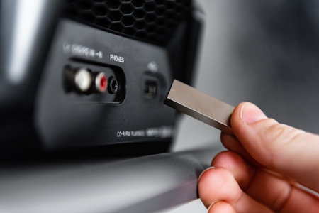 Hand holding silver USB flash drive connected to audio system or tape recorder