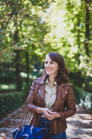 Smiling young beautiful brunette girl stands in autumn clothes in the park.