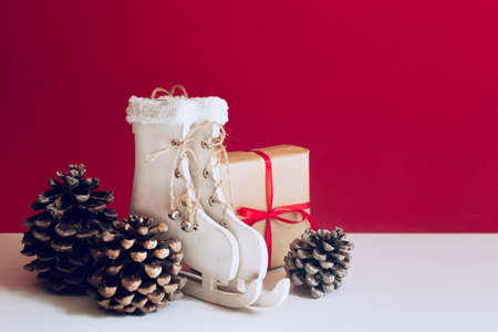 Christmas gift and decorations, wooden skates and pine cones are on a red background. Free space for...