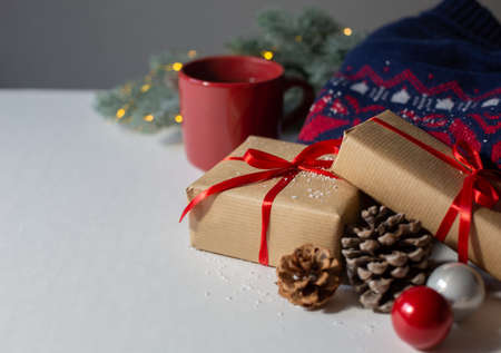 Christmas gifts wrapped in paper with a red ribbon, a warm sweater and a red mug with tea are on a...