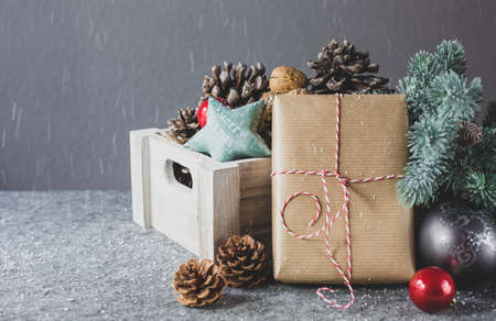 A wooden box with pine cones and Christmas decorations and gift in wrapping paper are on a table on...