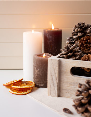 Three lighted candles and cedar cones in a wooden box and dry orange slices are on a light background.の写真素材