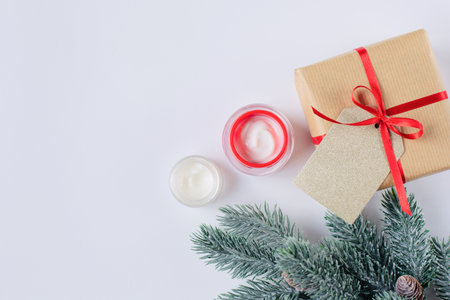 Cream in red jar as a Christmas present and a fir branches are on a white background. Free space for text.の写真素材