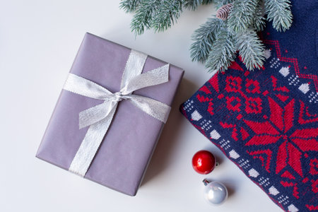 Gift wrapped in wrapping paper, a spruce branch, a warm sweater with a Christmas ornament.