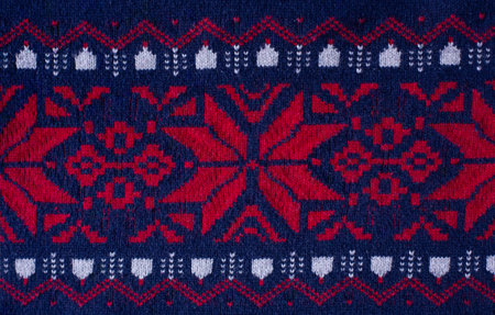 Background in the form of a blue knitted sweater with a red Christmas ornament.