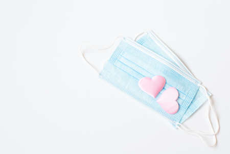 Two medical blue masks decorated with pink hearts are on a light background. The theme is Valentine's Day during a pandemic. Free space for text.の写真素材