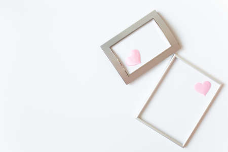 Two silver photo frames decorated with pink satin hearts are on a white background on the right side of the image. Valentine's Day or wedding theme. Free space for text.の写真素材