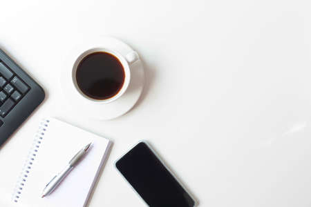 A white cup with black coffee, a mobile phone and a notebook with a pen and keyboard are on a white background. Business theme. A set of office utensils. Free space for text. View from the top point.の写真素材