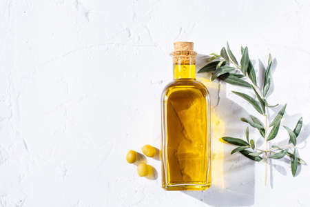 A glass bottle with olive oil and sprigs of an olive tree and olives are on a white background. Healthy food and healthy lifestyle theme. Copy space.の写真素材