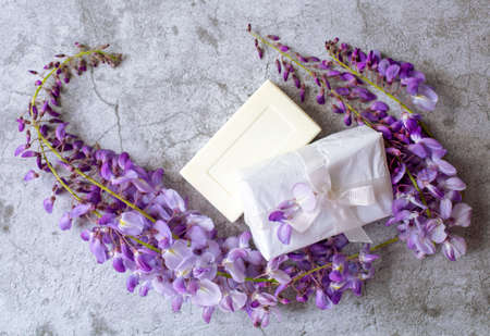 Toilet soap and a wrapped gift with a white ribbon surrounded by a blooming wisteria sprig are on a...