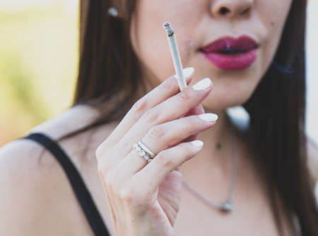 A girl with brightly painted lips are smoking a thin cigarette.の写真素材