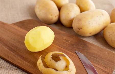 Peeled fresh potatoes on a cutting wooden board in the kitchen.の写真素材