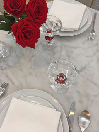 Fragment of a festively served table with red roses and glass wine glasses. Romantic date theme.