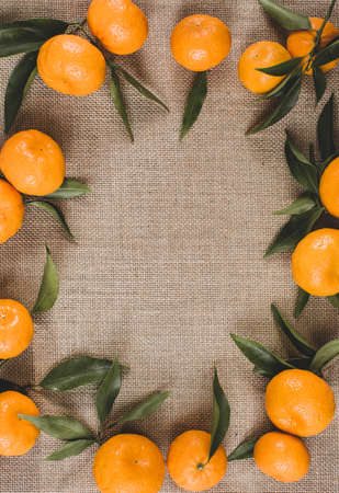 A background of burlap along the perimeter of which there are ripe tangerines with green leaves. Free space for text loops. Vertical image. View from the top point.の写真素材