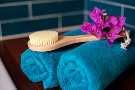 Two rolls of aquamarine terry towels, a beautiful flower and a wooden bath brush lie on the shelf in the bathroom against the backdrop of tiles. Spa theme.の写真素材
