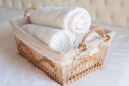 Three rolls of white terry towels lie in a wicker basket on a white background. Retro style.の写真素材