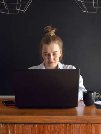 Young woman is working online on notebook while sitting on the kitchen at home or in the office. Concept of studying or working from home online. Vertical image.の写真素材
