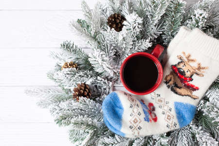 Warm woolen knitted socks with a New Year's pattern, a red cup with black coffee and spruce snow branches are on a white wooden background. Free space for text. View from the top point.の写真素材