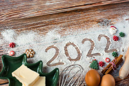 New Year's baking theme. Products, kitchen utensils for baking and the numbers 2022 are on a wooden...