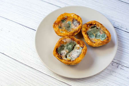 Three Three cakes with green mold are on a gray plate against a wooden surface.